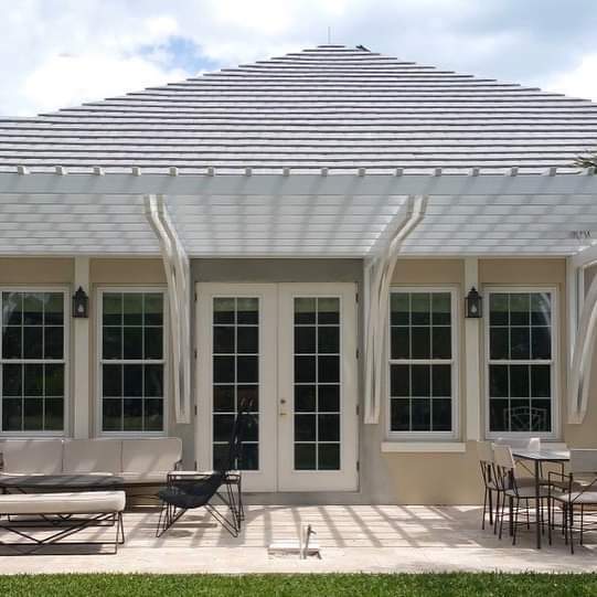 Custom white pergola covering back of tan house with white french doors
