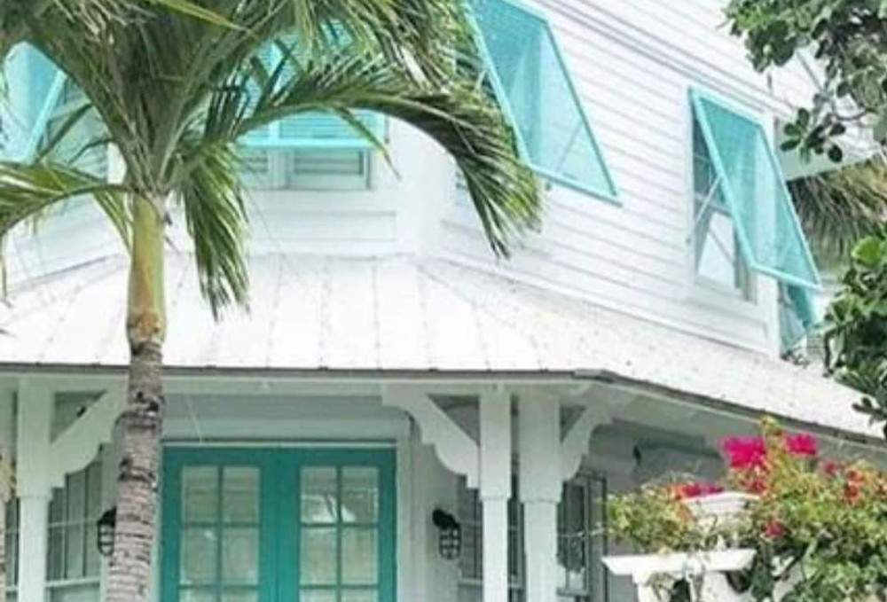 Aqua Bahama shutters on a white house with palm tree in front