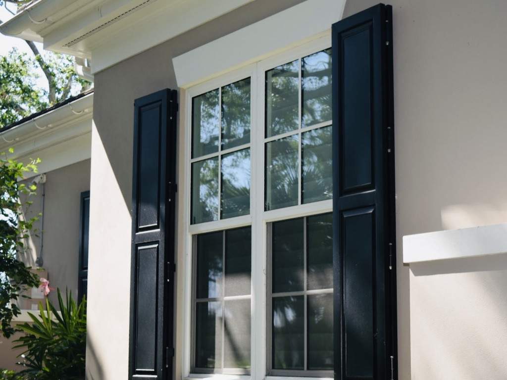 black colonial shutters around window of a taupe house with cream trim