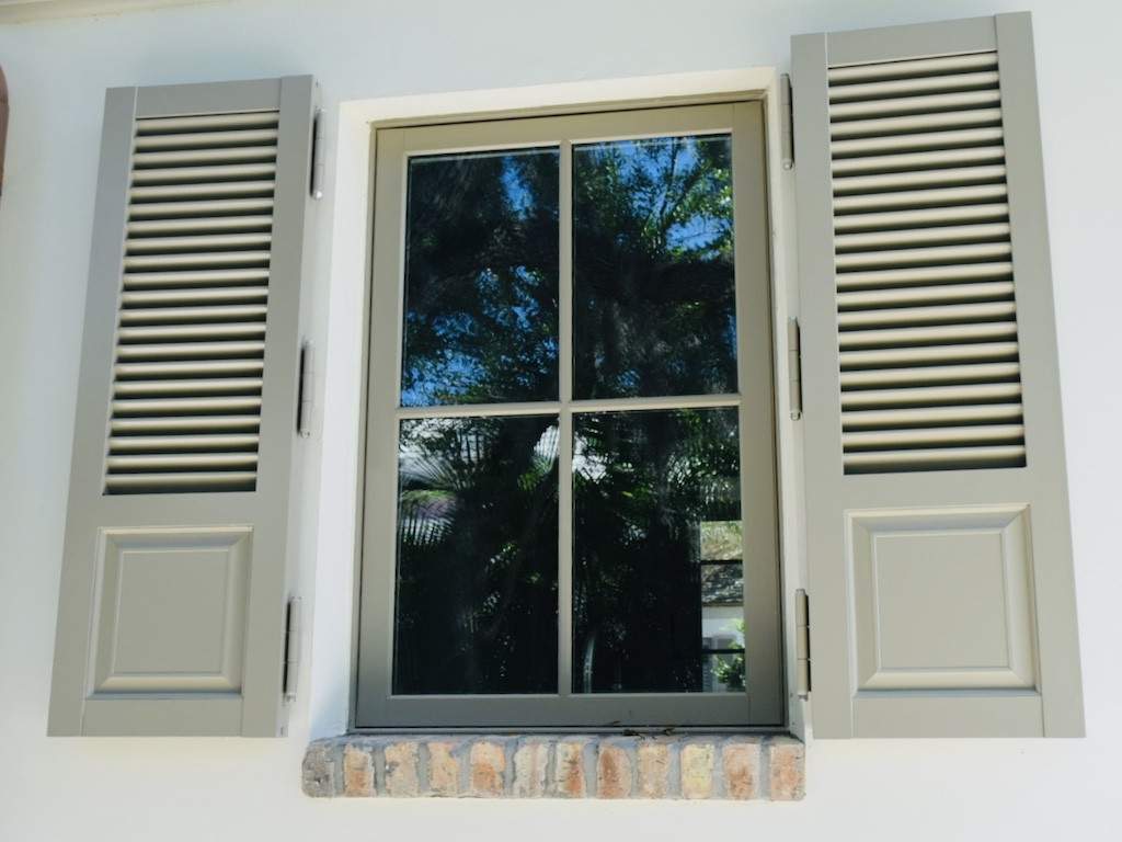 light brown colonial shutters around window with a brick window sill
